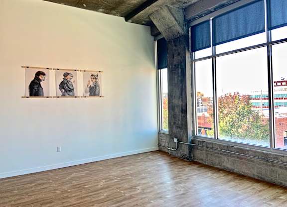 Three people are standing in front of a window in a room with wooden floors.