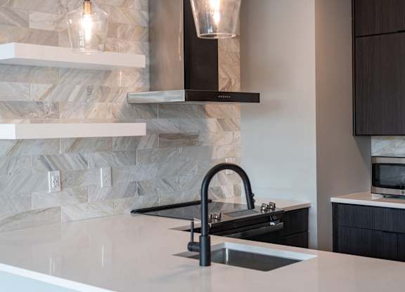 A modern kitchen with a stone backsplash and a black faucet.