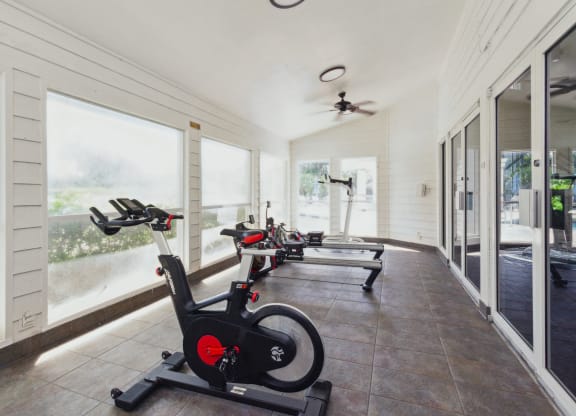 a row of exercise bikes in a room with windows at The Villages of Banyan Grove, Florida, 33436