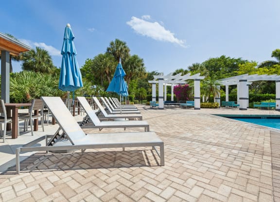 a pool with lounge chairs and umbrellas next to a pool at The Villages of Banyan Grove, Boynton Beach, 33436