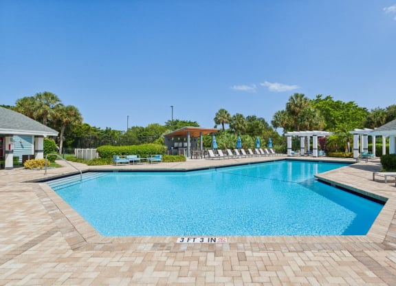a large swimming pool with chairs around it in front of a house at The Villages of Banyan Grove, Boynton Beach, FL