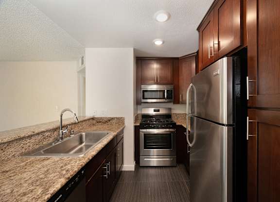 a kitchen with dark wood cabinets and granite countertops and stainless steel appliances at Croft Plaza Apartments, West Hollywood, CA