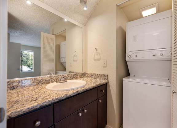 Bathroom with large mirror, granite vanity with sink and larger sized washer and dryer nearby at Fountains of Fair Oaks, California