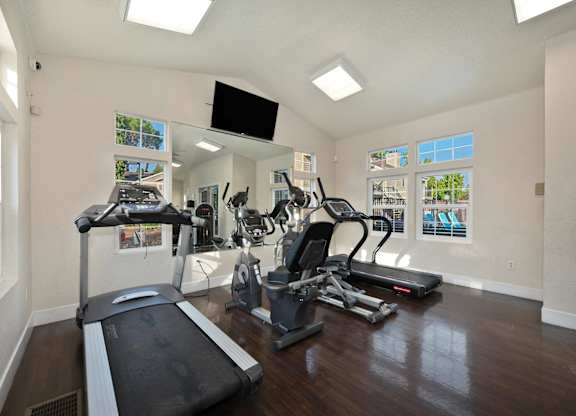 the gym has plenty of exercise equipment and a flat screen tv at Hidden Oaks Apartments, Citrus Heights, 95621
