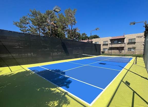 A tennis court with a blue and yellow surface and a black fence surrounding it.