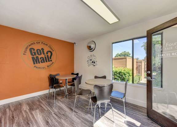 Parcel Room with Hardwood Inspired Floor, Short Round Tables, Chairs, Orange Wall with at Fountains of Fair Oaks, Fair Oaks