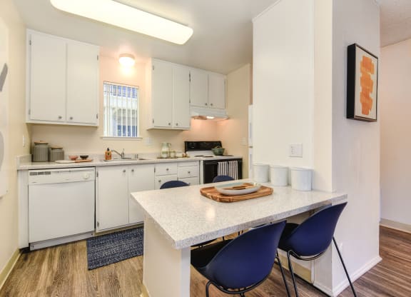 a kitchen with white cabinets and a white table with blue chairs at Renaissance Park Apartments, California, 95618