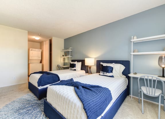 Model home bedroom with two beds and a desk with a chair. Stackable washer and dryer inside room at Renaissance Park Apartments, Davis, California
