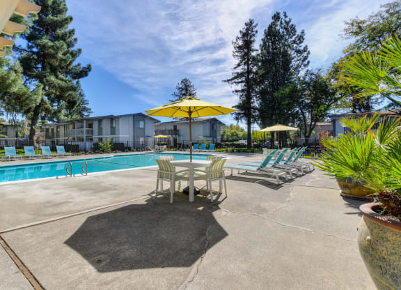 Community swimming pool area with tables, chairs and umbrellas for shade. at Renaissance Park Apartments, Davis, California