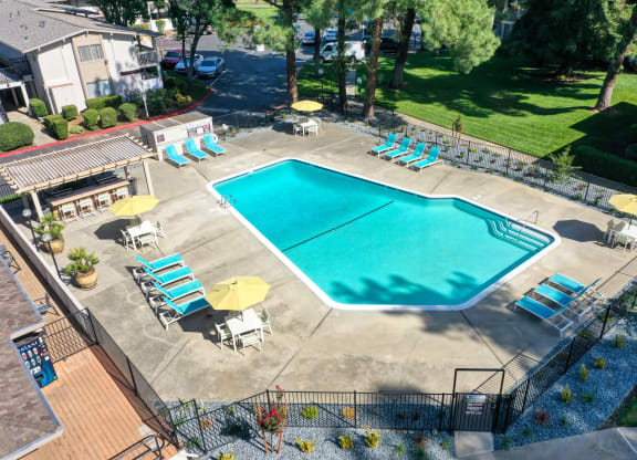 Drone photo of the community swimming pool area which is fenced and pool deck is filled with seating options. at Renaissance Park Apartments, Davis, CA, 95618
