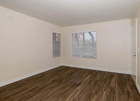 A room with wooden flooring and two windows with blinds.