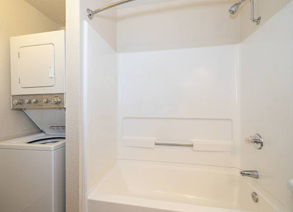 A white bathroom with a tub, toilet, and washing machine.