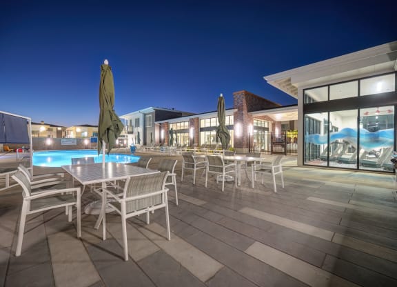 The swimming pool lounge area with tables, chairs and umbrellas at night.