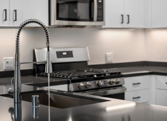 a kitchen with a sink with a gooseneck style faucet with water turned on and a stove in the distance
