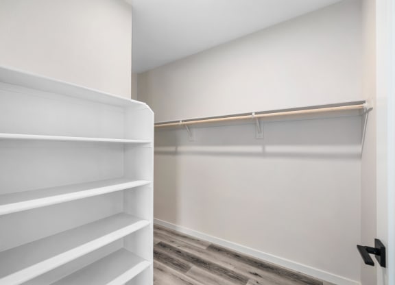 a walk in closet with white shelves and a wood floor