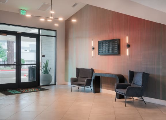 a lobby with chairs and a table in front of a glass door