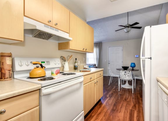 Model home kitchen with hardwood inspired flooring , white kitchen appliances, and dining area with ceiling fan at Vineyard Terrace Apartments, California