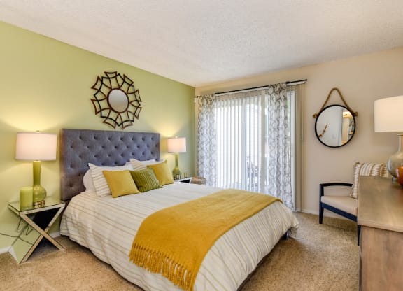 Model home bedroom with queen size bed, carpeting, nightstands and dresser with patio door on one side of room at Vineyard Terrace Apartments, Napa, CA, 94558