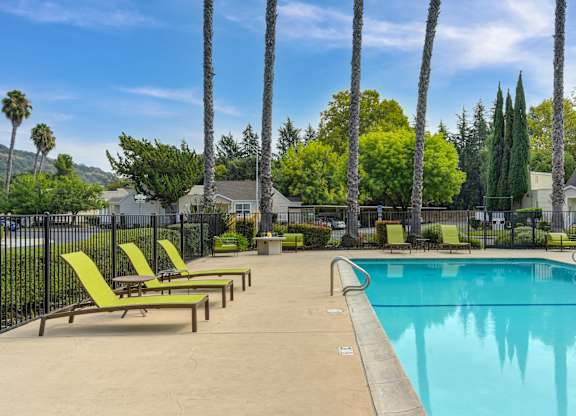 A pool surrounded by palm trees and lounge chairs at Vineyard Terrace Apartments, California