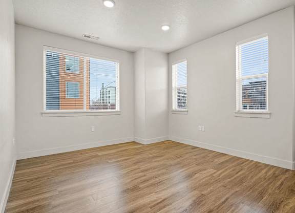 Empty room with wooden floors and two windows.