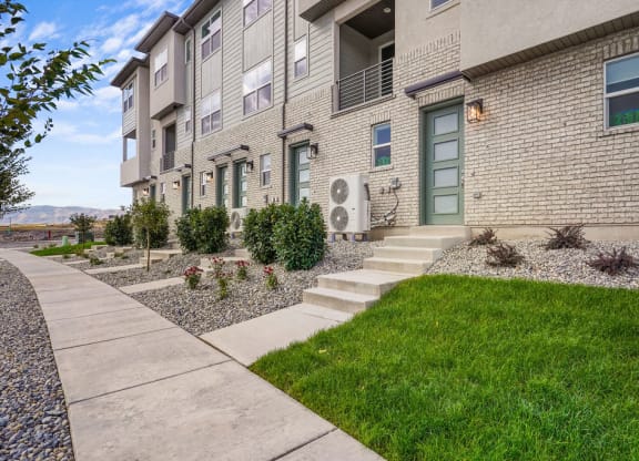 a sidewalk in front of an apartment building with grass and plants
