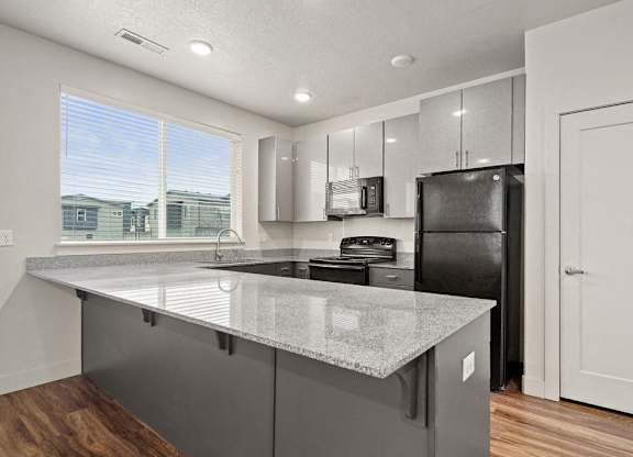 A kitchen with a black refrigerator and a granite countertop.
