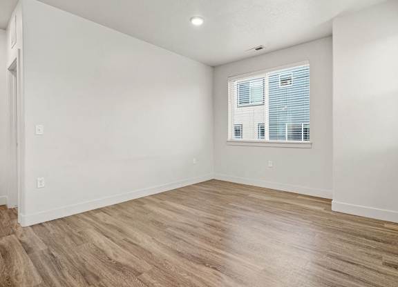 A room with wooden flooring and a window with blinds.
