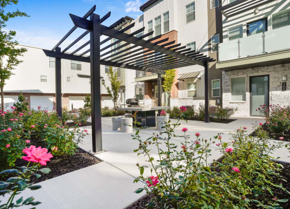 a patio with flowers and a pergola in front of an apartment building