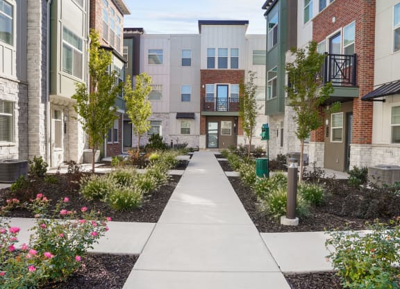 a sidewalk in front of an apartment complex with plants and trees