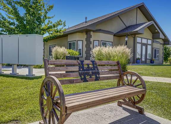 A wooden bench with a wagon wheel design is in front of a house.