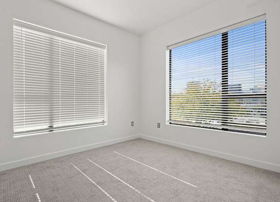 an empty room with two windows with blinds and