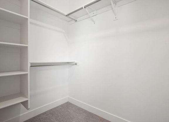 a walk in closet in a white room with shelves