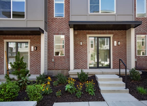 Front of a building with stairs and plants at Greens by Lotus Townhomes, Ogden, 84403