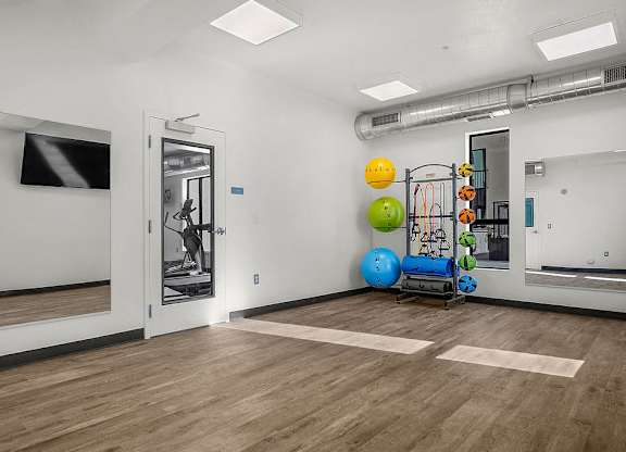 A gym with a variety of equipment including a treadmill, exercise balls, and a weight machine.