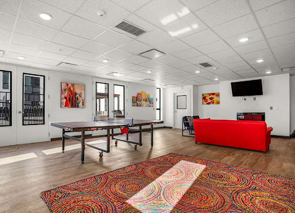 A room with a red couch and a table with a red cushion.