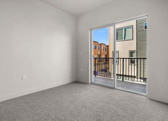A room with a carpeted floor and a sliding glass door leading to a balcony.
