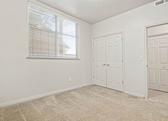 A room with a window, carpeted floor, and two doors.