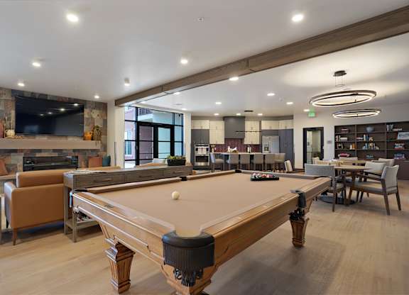 A pool table is in the middle of a room with a bar and a TV.