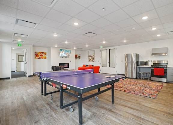 A ping pong table is in the middle of a room with a kitchen area in the background.