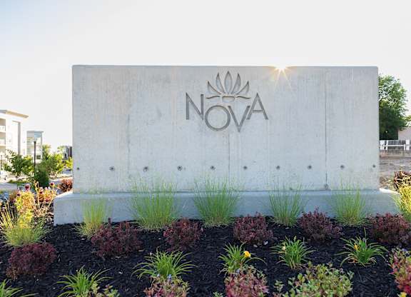 A concrete sign with the word NOVA on it is surrounded by plants.