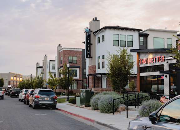 A street with cars parked on the side and a Thai Better restaurant on the right.