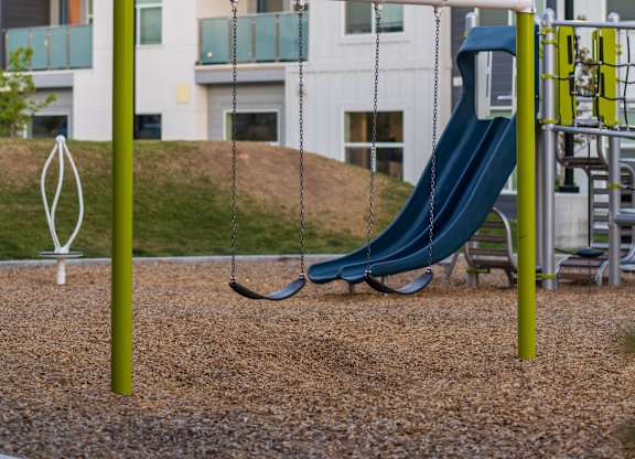 A playground with a slide and swings in front of a building.