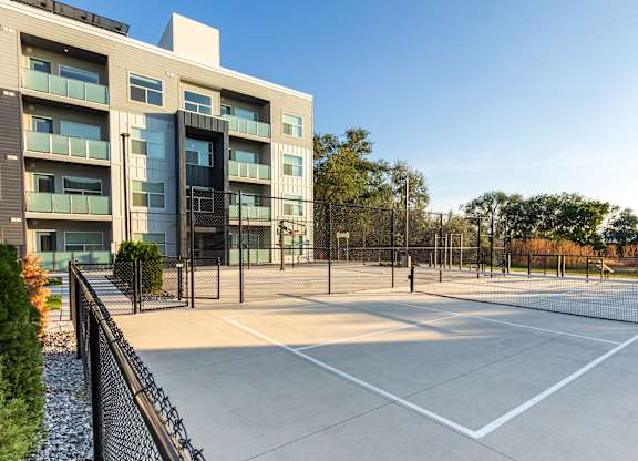 A tennis court is located in front of a modern building.
