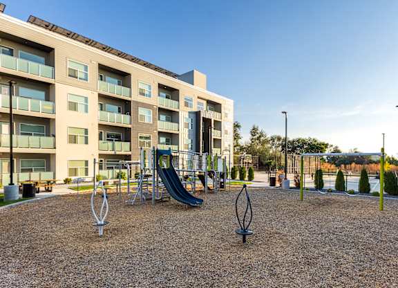 A playground with a slide and swings in front of apartment buildings.