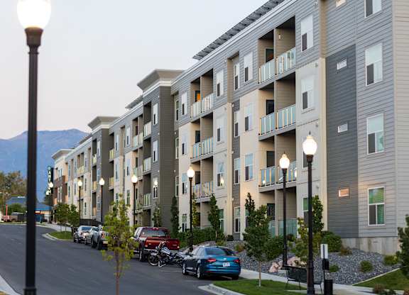 A street view of a residential area with cars parked on the side of the road and apartment buildings in the background.