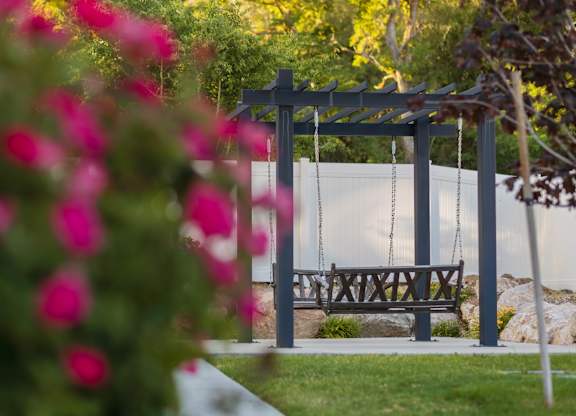A swing set in a park with a bench and flowers in the foreground.