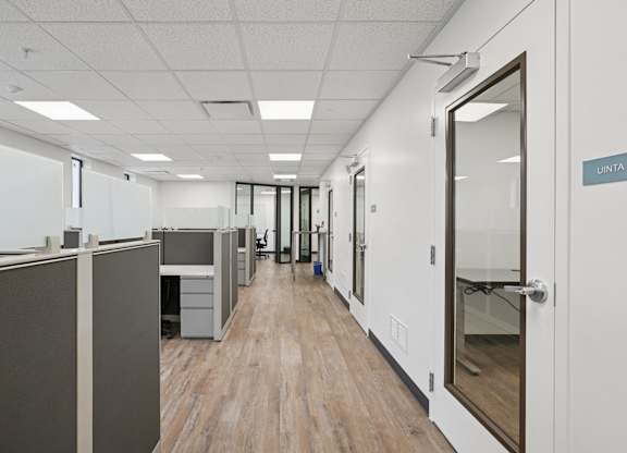A hallway with cubicles on the left and doors on the right.