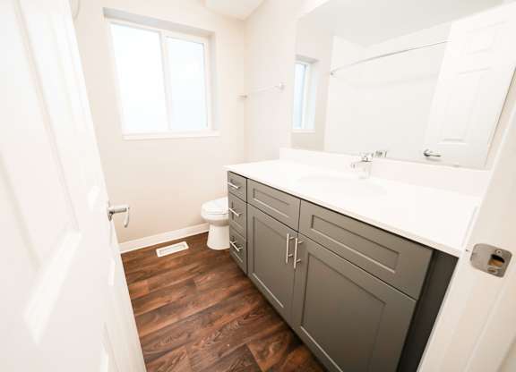 A bathroom with a toilet, sink, and wooden floors.