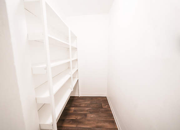 A long white shelving unit with multiple shelves is in a room with wooden floors.