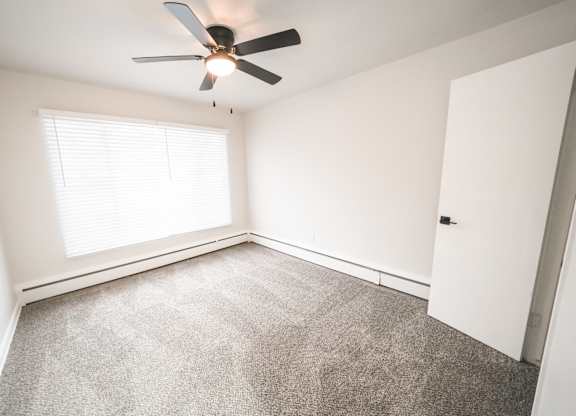 A room with a ceiling fan and a window with blinds.